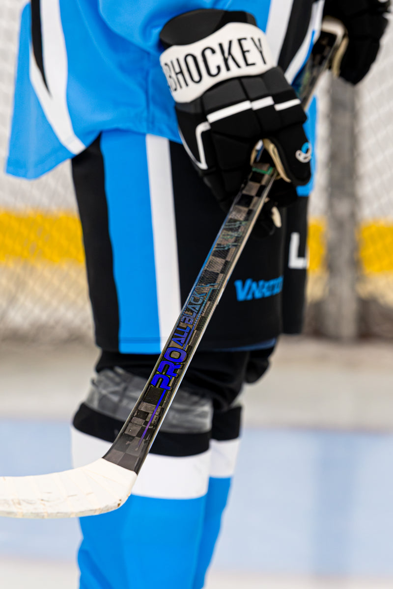 Détail du bâton de hockey Pro All Black V2 de LabSports près des patins d’un joueur